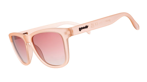 Three-quarter angle view of blush pink wayfarer-shaped sunglasses with pink gradient lenses.