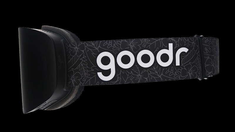 Side view of black snow goggles with an adjustable black strap with the goodr logo over a faintly outlined tropical pattern.