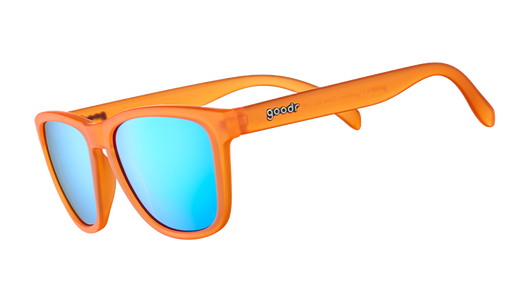 Three-quarter angle view of translucent bright orange sunglasses with blue reflective lenses on a white background.