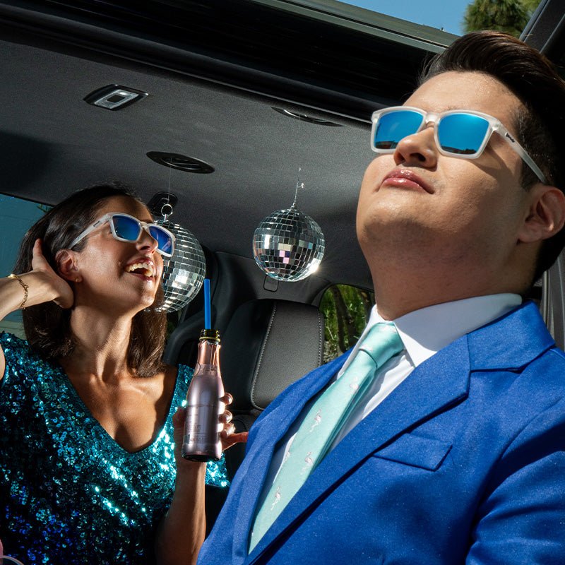 A man and woman in slim-fit clear sunglasses with reflective blue lenses smile beneath disco balls in a party limo.
