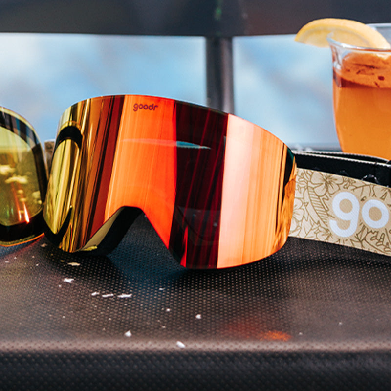 Three-quarter angle view of green snow goggles with a bright orange lens next to a swappable magnetic lowlight amber lens.