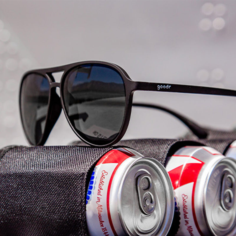Three-quarter angle view of black aviator sunglases with non-reflective black lenses sitting atop beer cans in a utility holster.