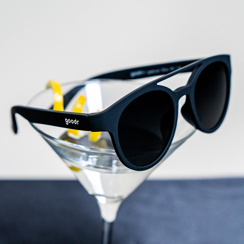 Three-quarter angle view of round black sunglasses with a double bridge and black lenses sitting on a martini glass.