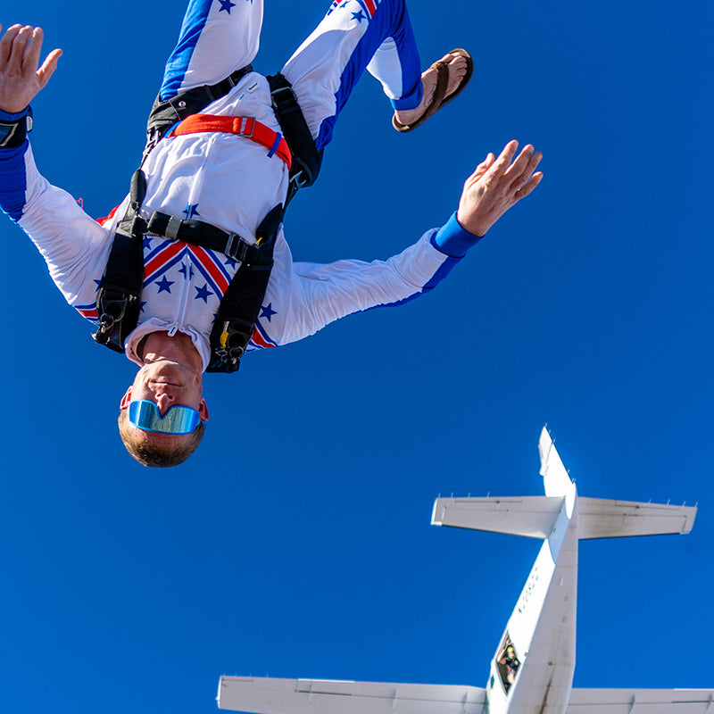 A skydiver jumps out of a plane wearing red, white, and blue sunglasses that stay perfectly put on his face.