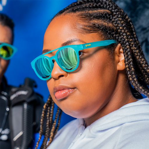 A stylish woman wears aqua blue double nose bridge round sunglasses with blue reflective circle lenses.