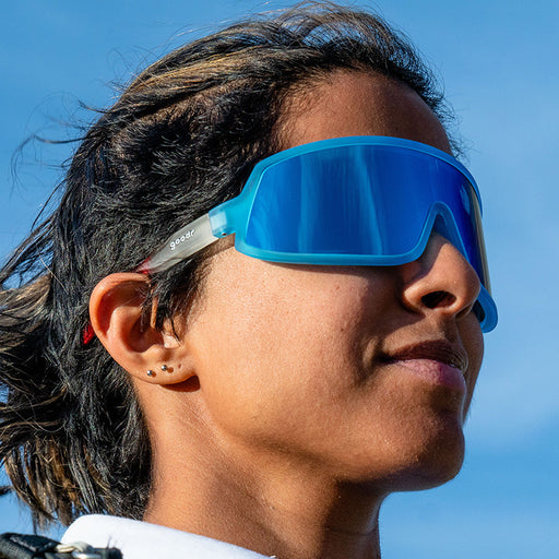 A woman wearing epic red, white, and blue sunglasses with a single blue wraparound lens looks confidently into the sky.