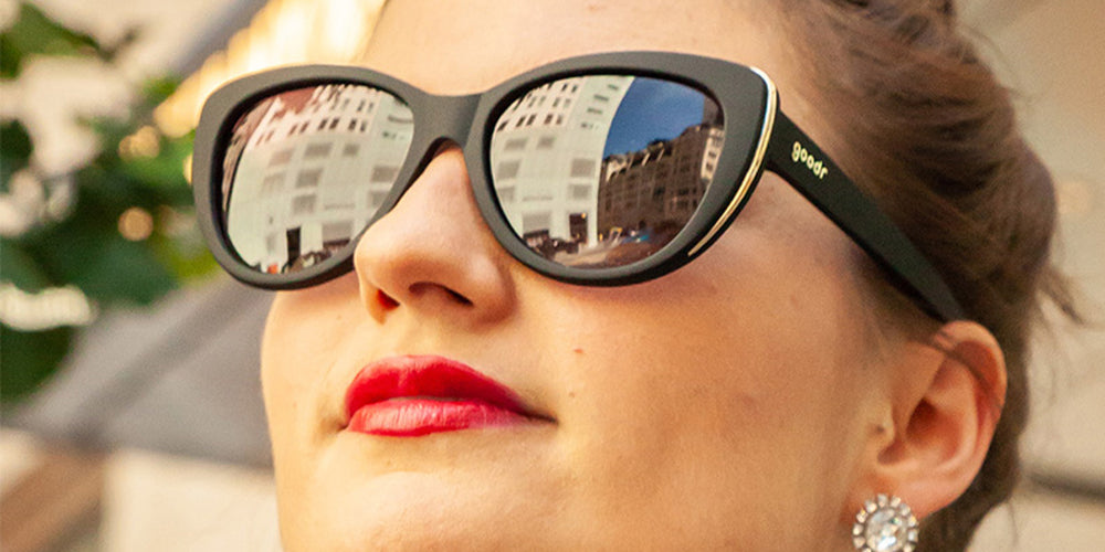 Close-up of a person wearing black goodr sunglasses with a city reflection.