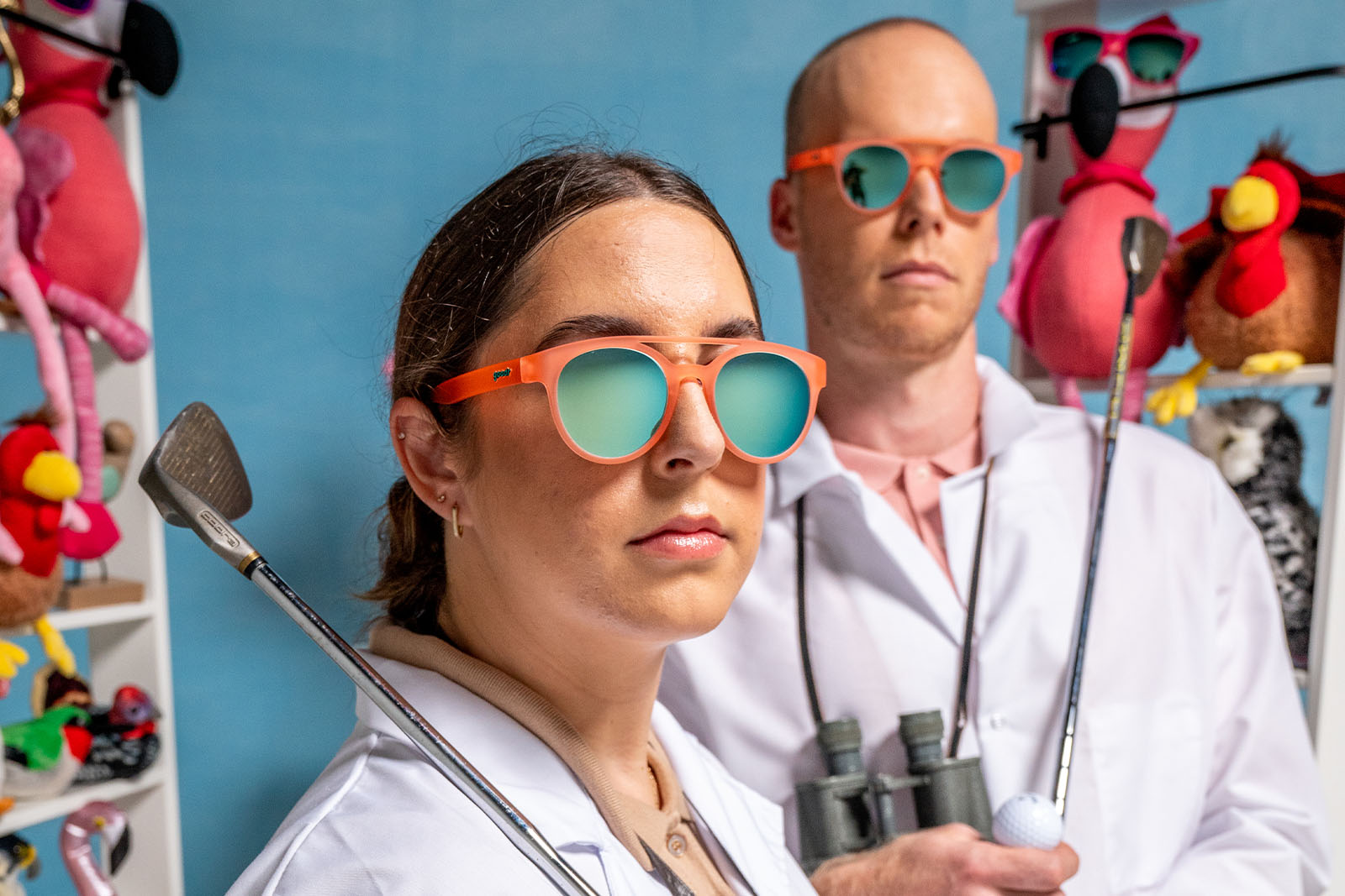 Two people wearing orange goodr sunglasses, one holding golf clubs.