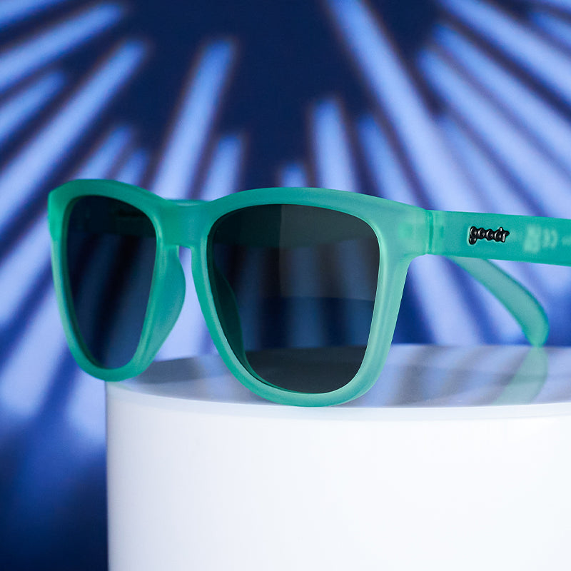 Three-quarter angle view of mint green square-shaped sunglasses atop a white display.
