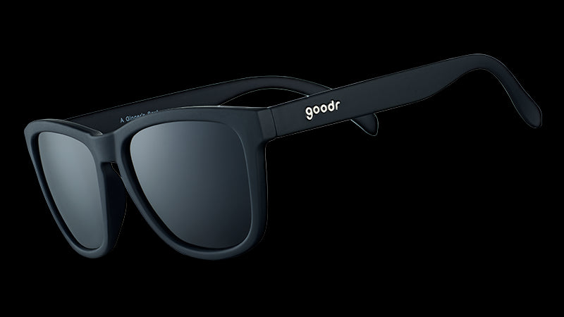 Three-quarter angle view of square-framed black sunglasses with black lenses on a white background.