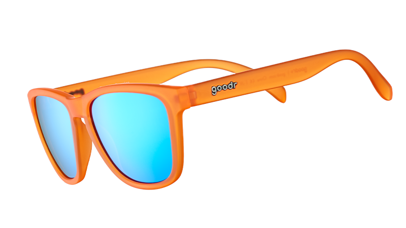 Three-quarter angle view of translucent bright orange sunglasses with blue reflective lenses on a white background.