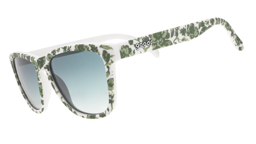 Three-quarter angle view of sunglasses with a green and white floral toile and green gradient lenses.