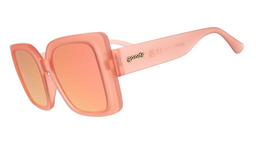 Three-quarter angle view of oversized square sunglasses in coral pink with champagne gold reflective lenses.