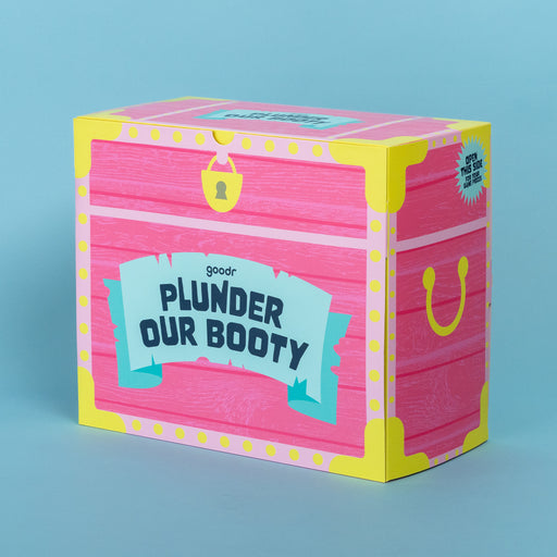 Three-quarter view of pink cardboard Plunder Our Booty game box, which resembles a treasure chest, sitting on blue backdrop.