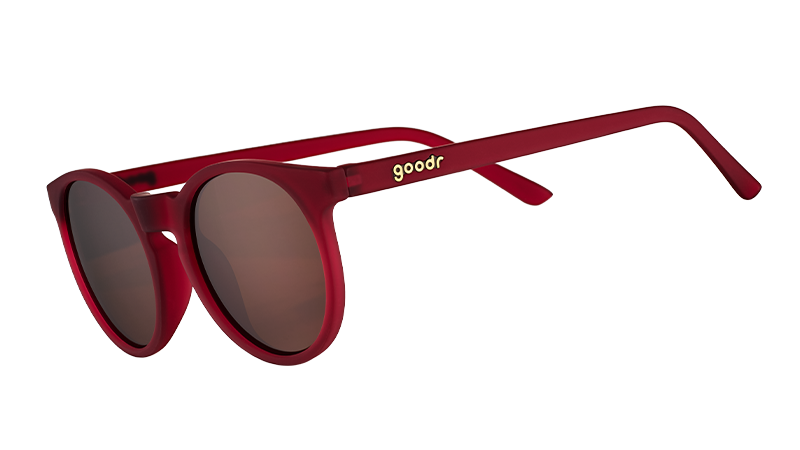 Three-quarter angle view of round burgundy sunglasses with circle-shaped non-reflective brown lenses.