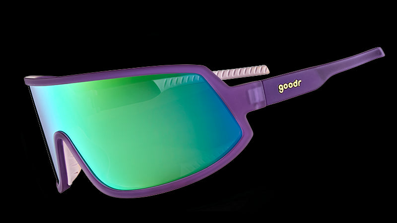 Three-quarter angle view of wraparound sunglasses with a reflective green lens and purple frames with white silicone inner grips.