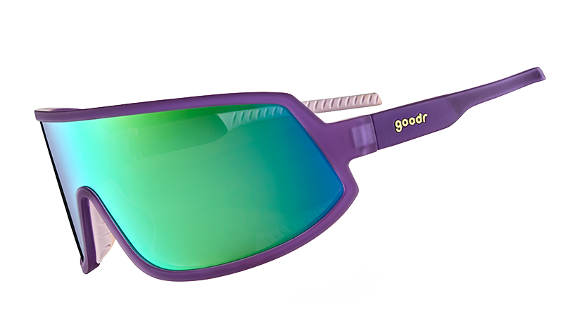 Three-quarter angle view of wraparound sunglasses with a reflective green lens and purple frames with white silicone inner grips.