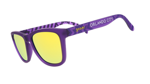 Angled view of shades tilted down. Purple frames w/ stripes + Orlando City on temples. Violet reflective lenses.