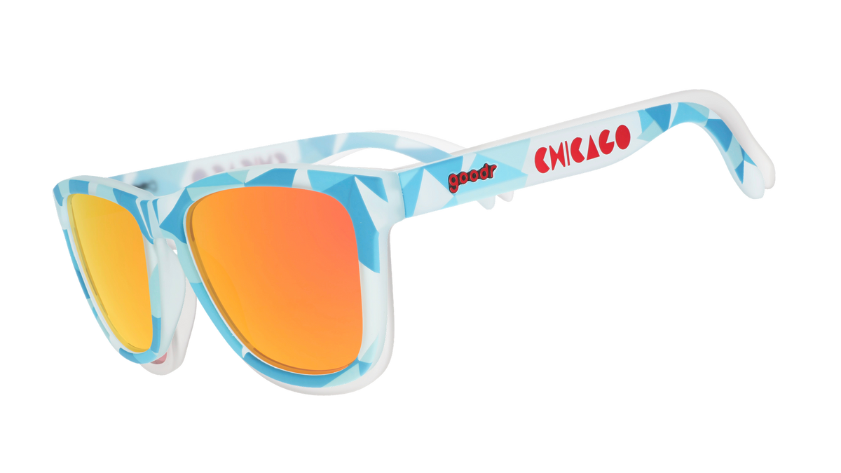 Three-quarter angle view of translucent blue, geometric-patterned sunglasses with burnt orange reflective lenses and Chicago logo.