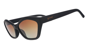 Three-quarter angle view of black geometric cat-eye sunglasses with amber gradient lenses against a white background.