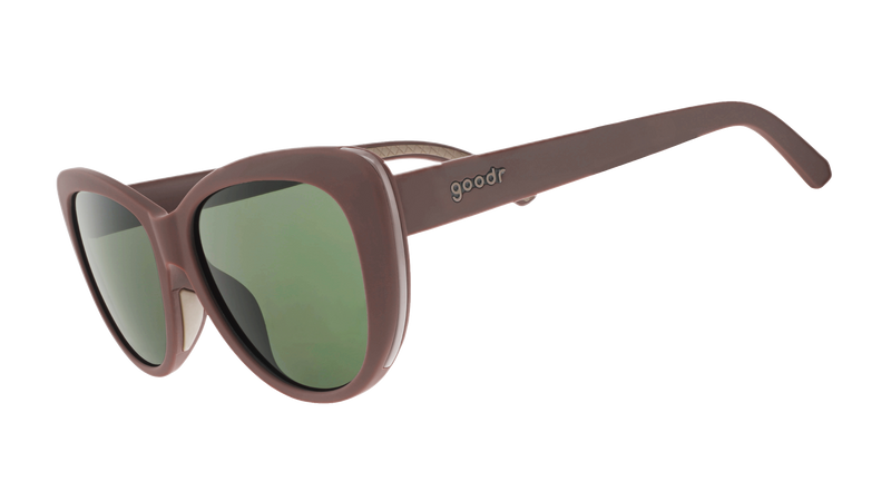 Two pairs of goodr sunglasses with matte brown frames and dark lenses, stacked on a gray knit sweater with a blurred autumnal background.