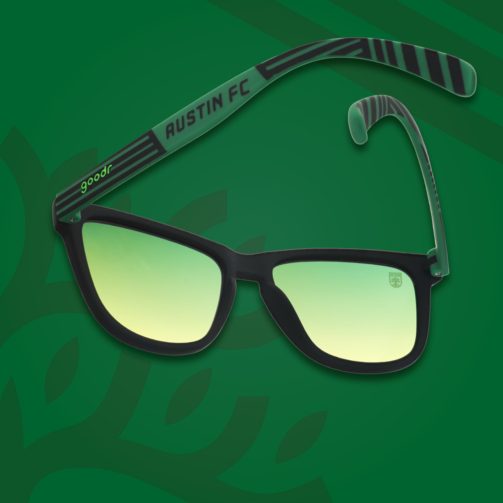 Three-quarter angle view of Austin FC shades tilted down. Green and black frames. Green-yellow lenses. Green background.