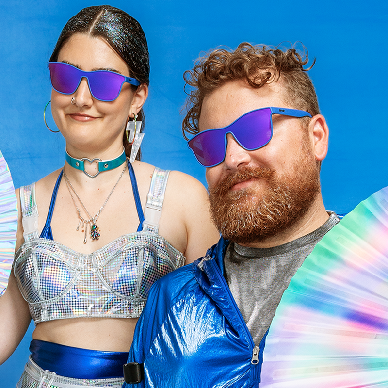 A man and a woman wearing metallic silver and blue clothing, wearing single lens blue and purple sunglasses.