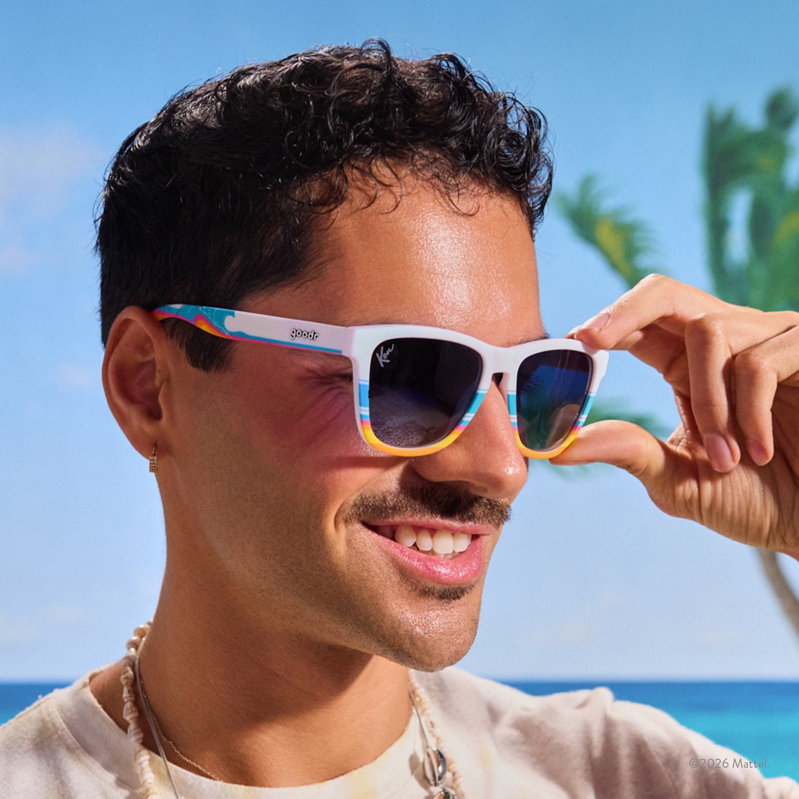 Close-up of a young man in a beach-like setting wearing white sunnies with a beach-inspired design and blue gradient lenses.