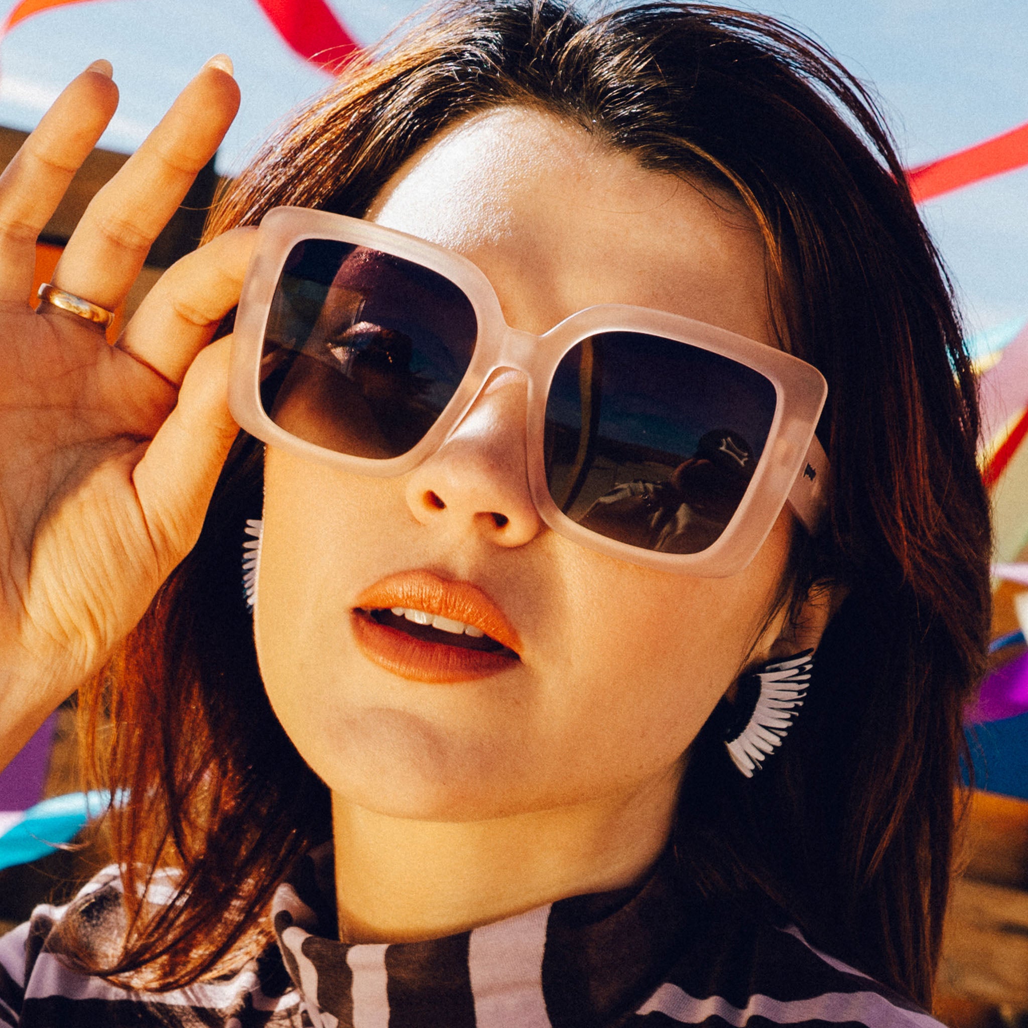Front view of a stylish young brunette woman wearing oversized square taupe sunglasses relaxing at a music festival.