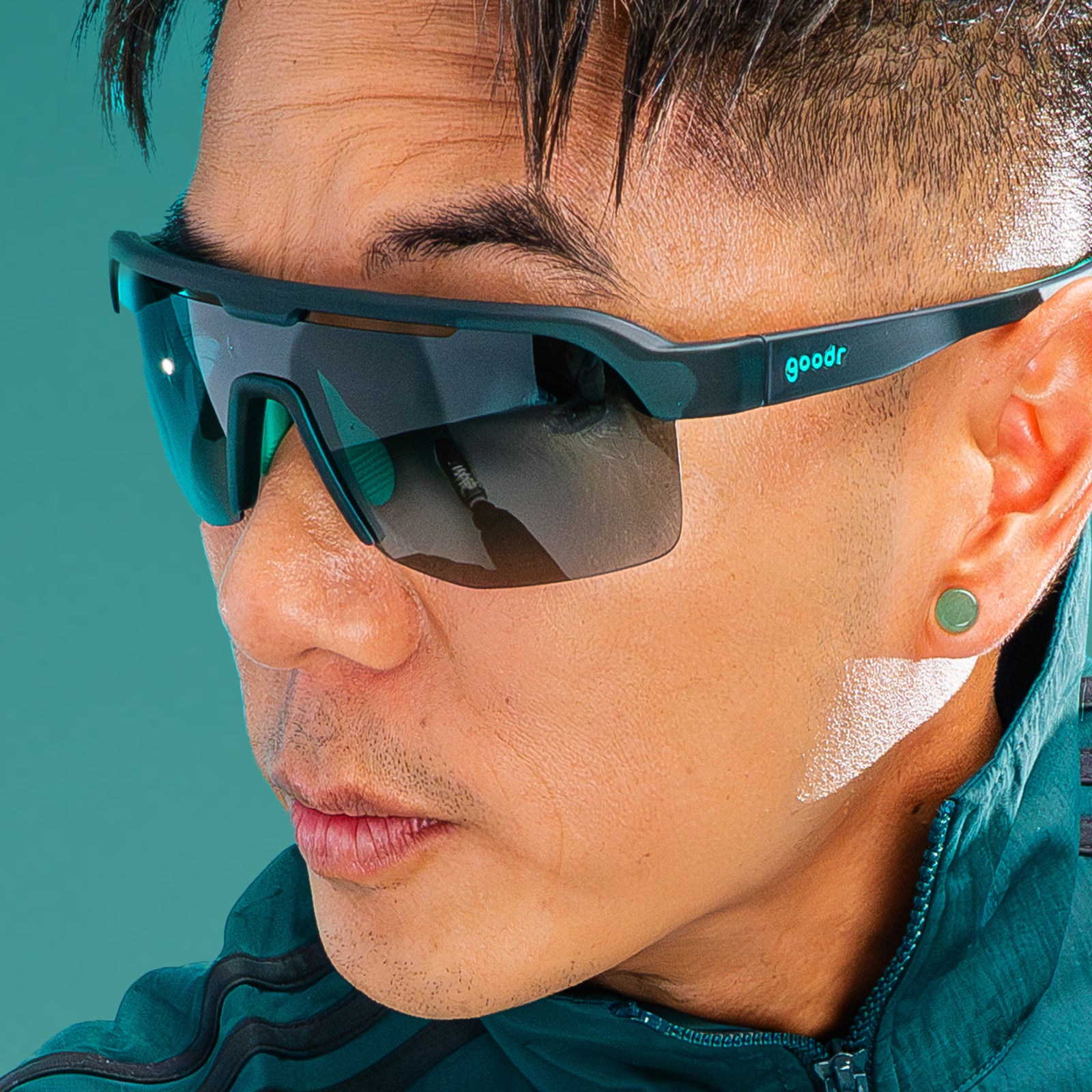 Profile view of a younger man with dark hair and an edgy haircut wearing dark teal Bolt Gs with green gradient lenses.