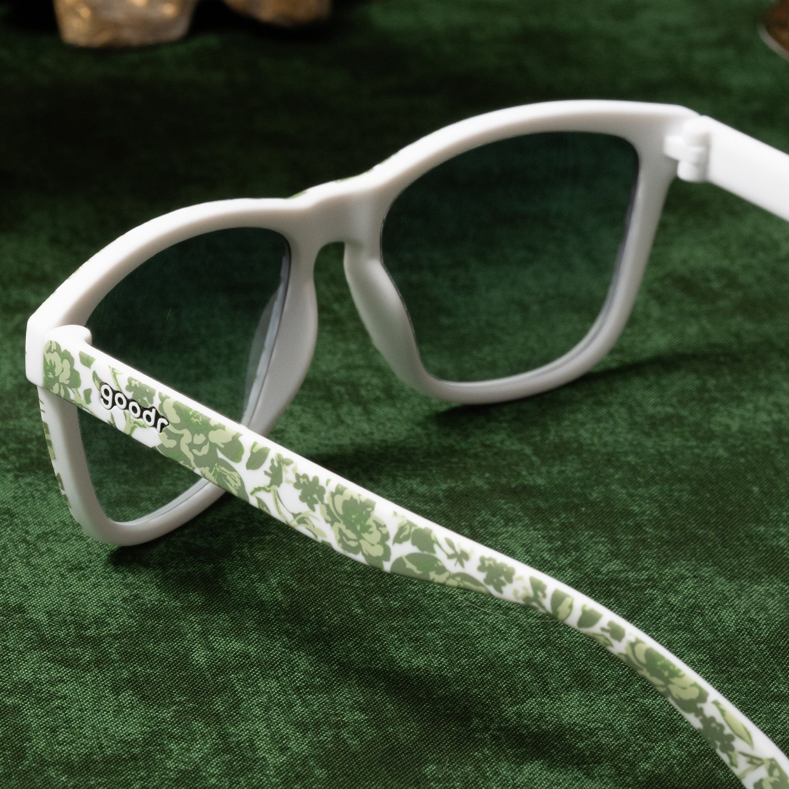 Back view of sunglasses with a green and white floral toile and green gradient lenses on a green tablecloth.