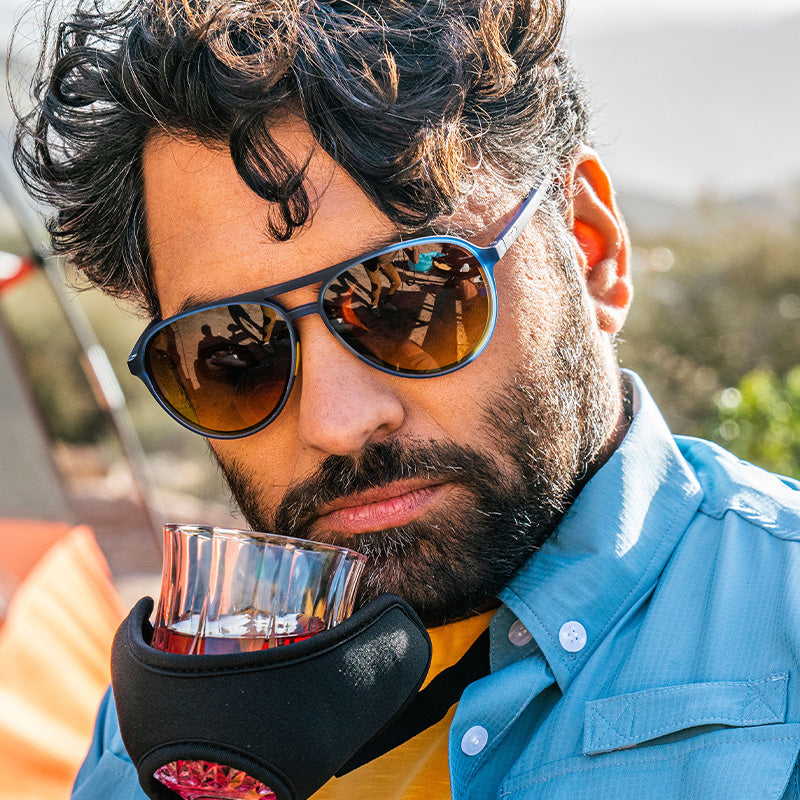 A bearded man in blue aviator sunglasses sniffs whiskey from a glass-holding contraption one might see in a Skymall catalog.