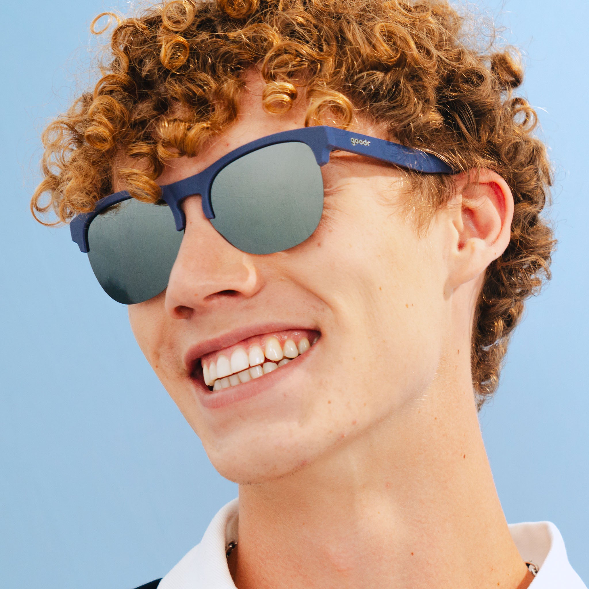 A stylish man wearing matte navy blue half-rim sunglasses with chrome reflective lenses smiles wide for the camera.