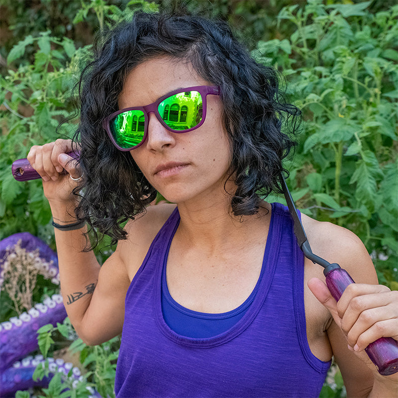 A woman wearing purple sunglasses with green lenses fiercely holds gardening tools, an octopus tentacle behind her.
