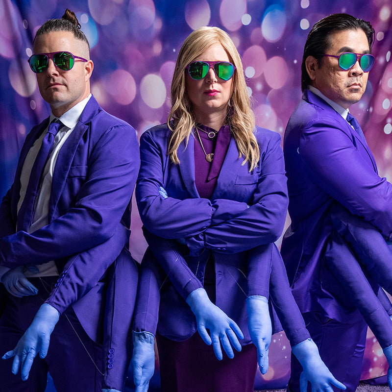 Three people in purple aviator sunglasses with green lenses cross their arms, fake arms sewn in each of their matching suits.