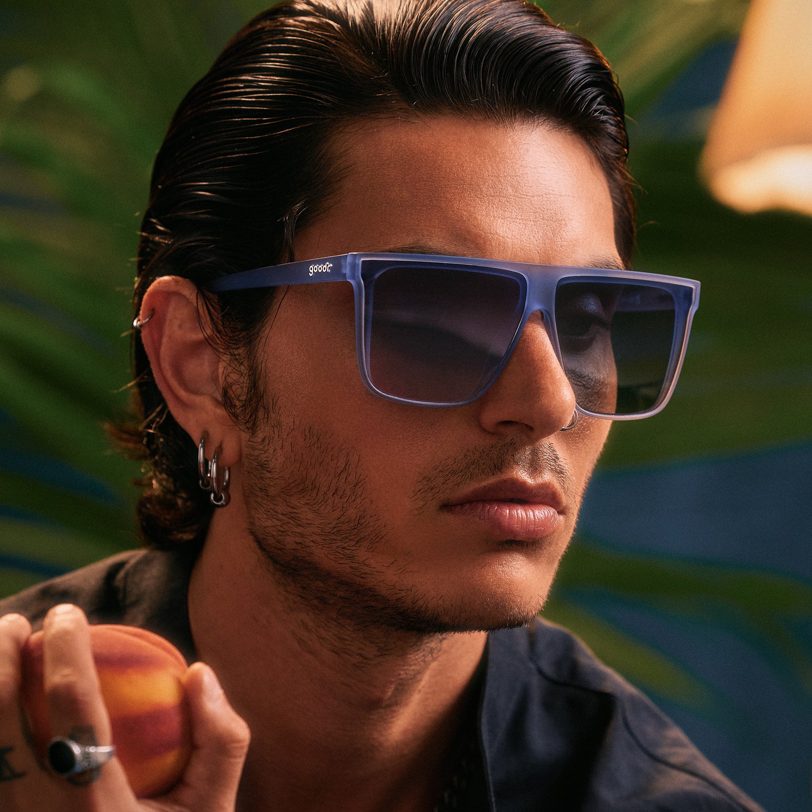 Close-up of a handsome young man with dark hair posing in oversized, dusty blue Fly G sunglasses with blue gradient lenses.