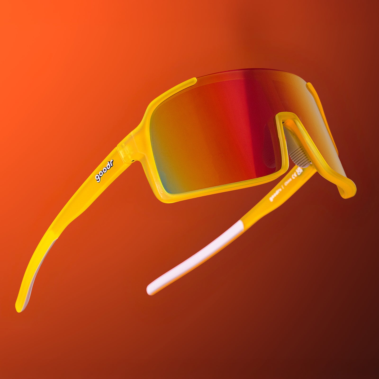 Yellow wrap sunglasses with red reflective lenses floating against a red ombre backdrop.