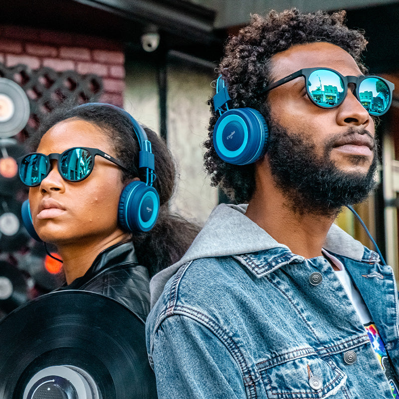 A hipster man and woman back-to-back, wearing big blue headphones and round black sunglasses with blue reflective lenses.