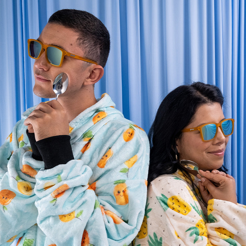 A man and woman in pajamas wearing small orange sunglasses smile as they cuddle their precious spoons.