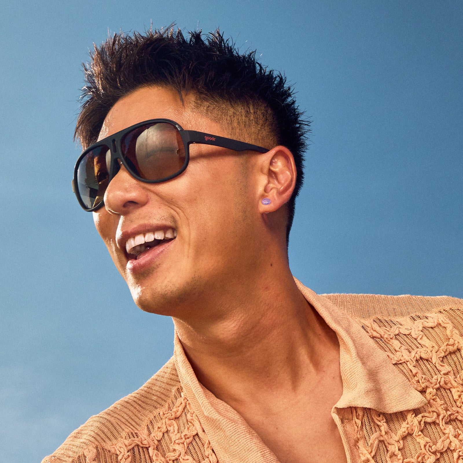 Side profile of a smiling man wearing black aviator sunglasses with amber gradient lenses.