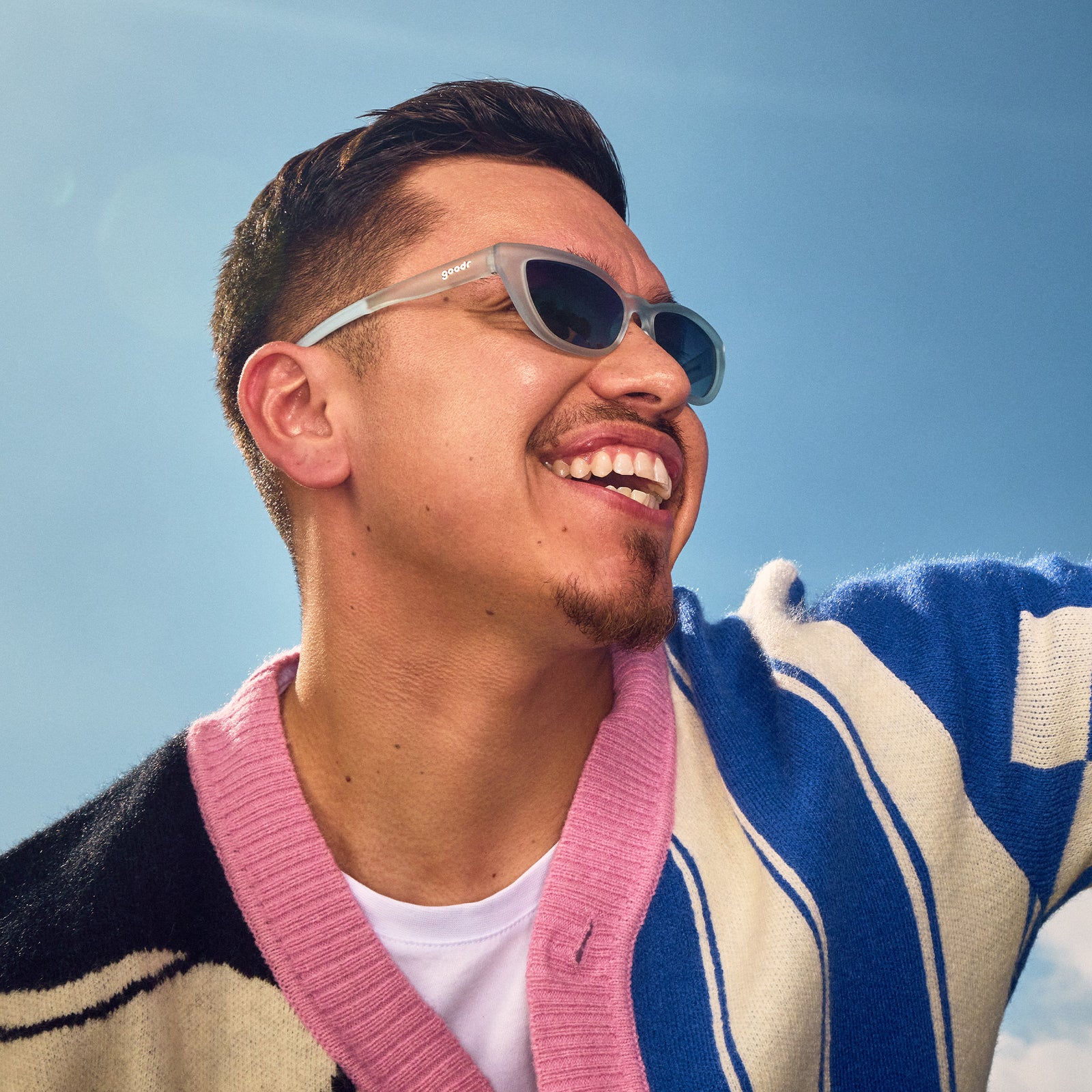 A smiling man poses with light blue cat-eye sunglasses with gradient violet lenses.