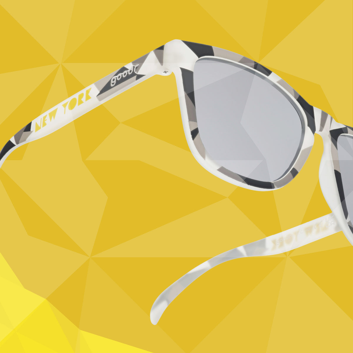 Translucent gray sunglasses with a tonal geometric pattern against a yellow geometric-patterned background.