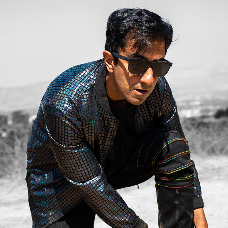 A man wearing black flat single-lens sunglasses and a futuristic dark reflective jacket lunges, looking ahead.