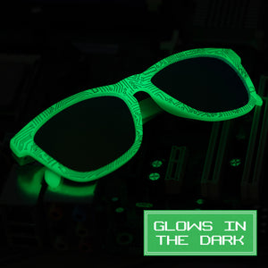 Green glow-in-the-dark sunglasses with a circuit-like pattern on the frame, set against a dark background with the label "GLOWS IN THE DARK.