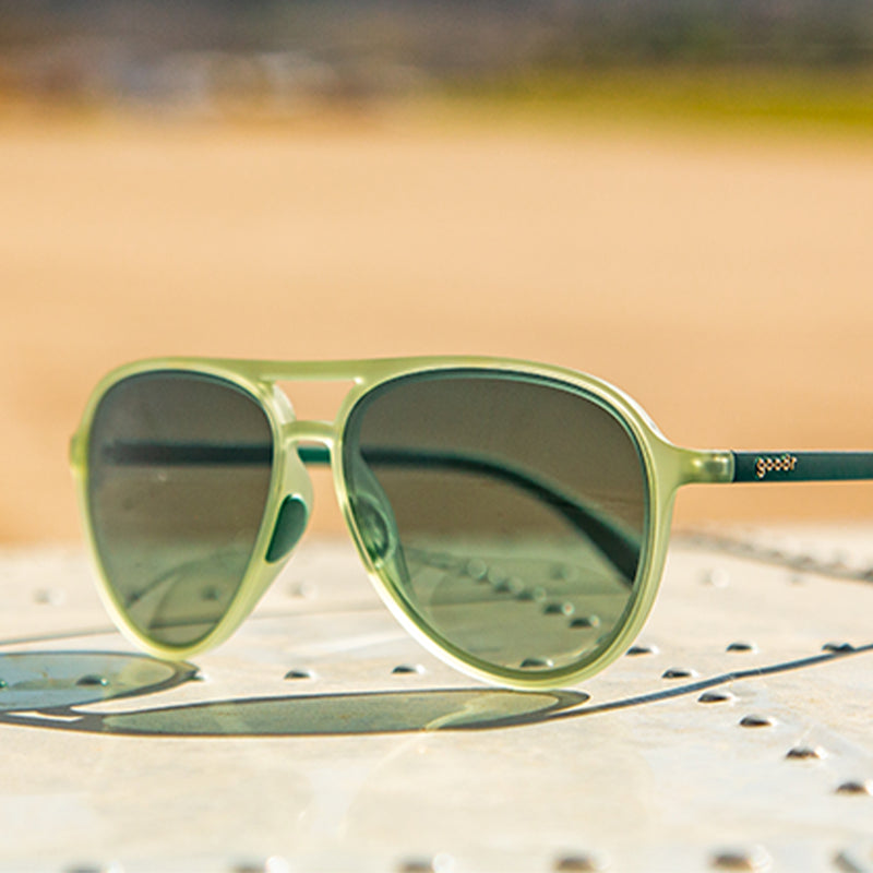 Three-quarter angle view of cadet green aviator sunglasses with green gradient lenses sitting atop riveted sheet metal.