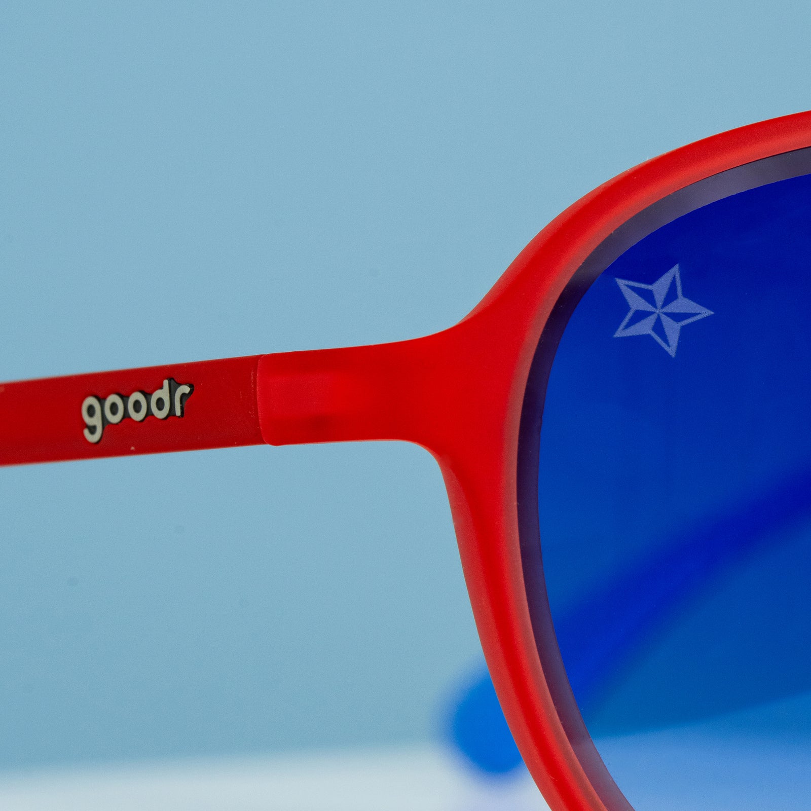 Three-quarter angle close-up view of aviator shades. Red front frame. Blue gradient lenses. Star etch on top right lens.