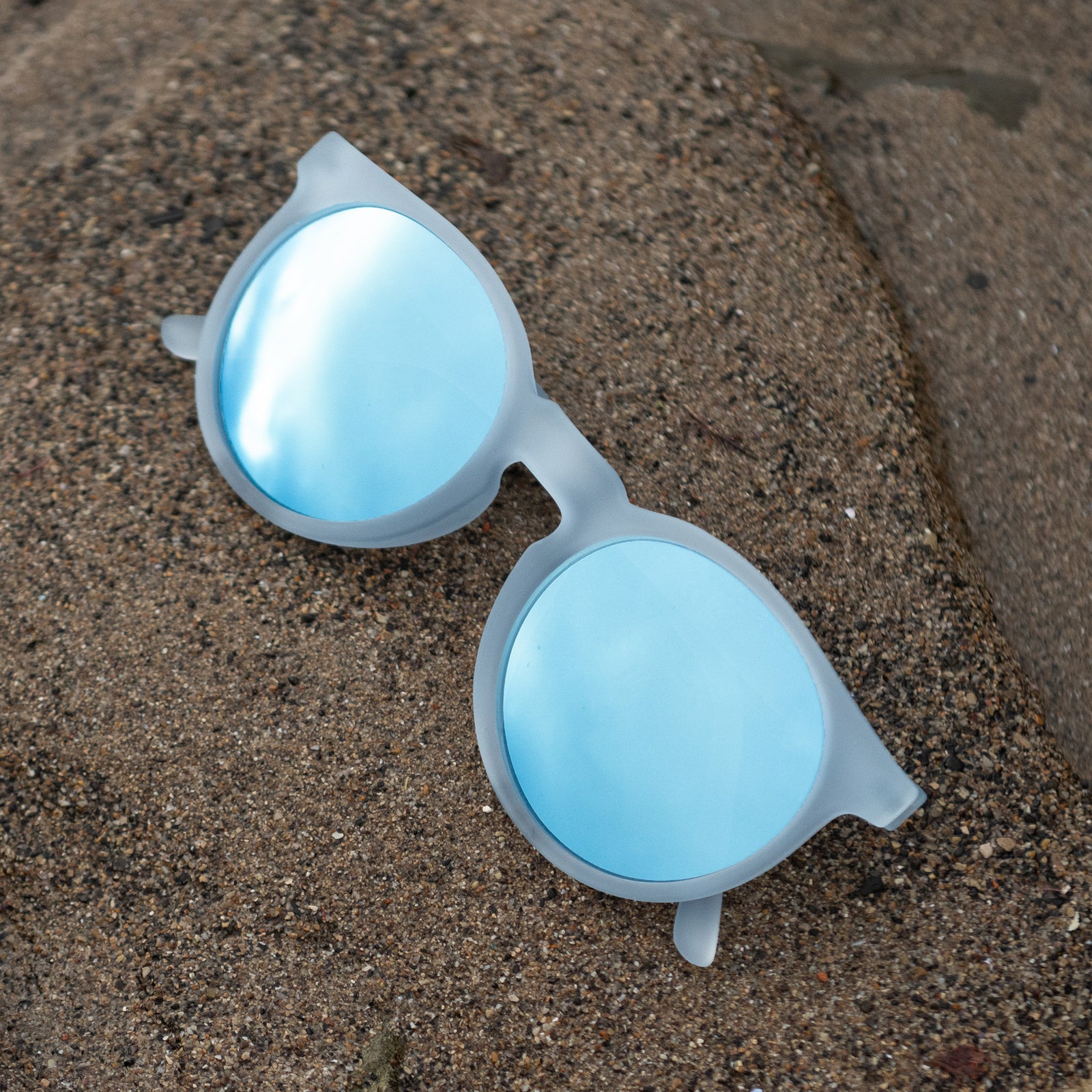 Translucent blue-gray Circle Gs with ice blue reflective lenses lying atop wet sand.