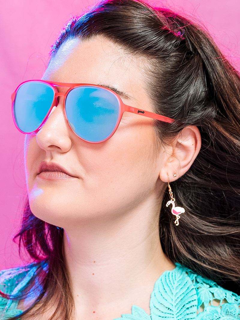 Woman wearing Carl Is My Co-Pilot sunglasses with flamingo earring, teal lace garment, and pink background.