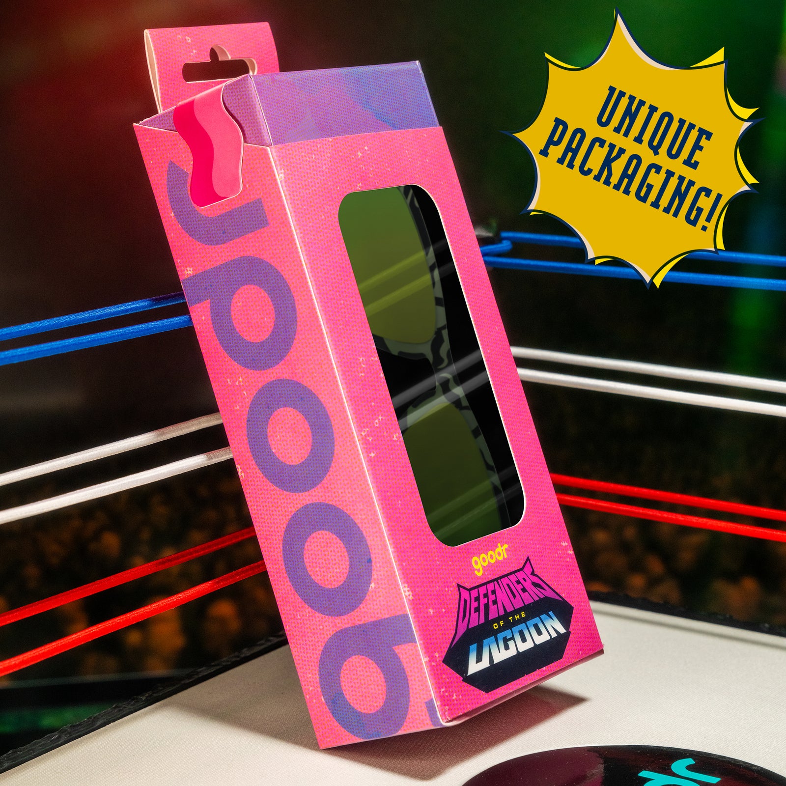 A hot pink and purple sunnies box that says Defenders of the Lagoon is posed in the corner of a miniature wrestling ring.