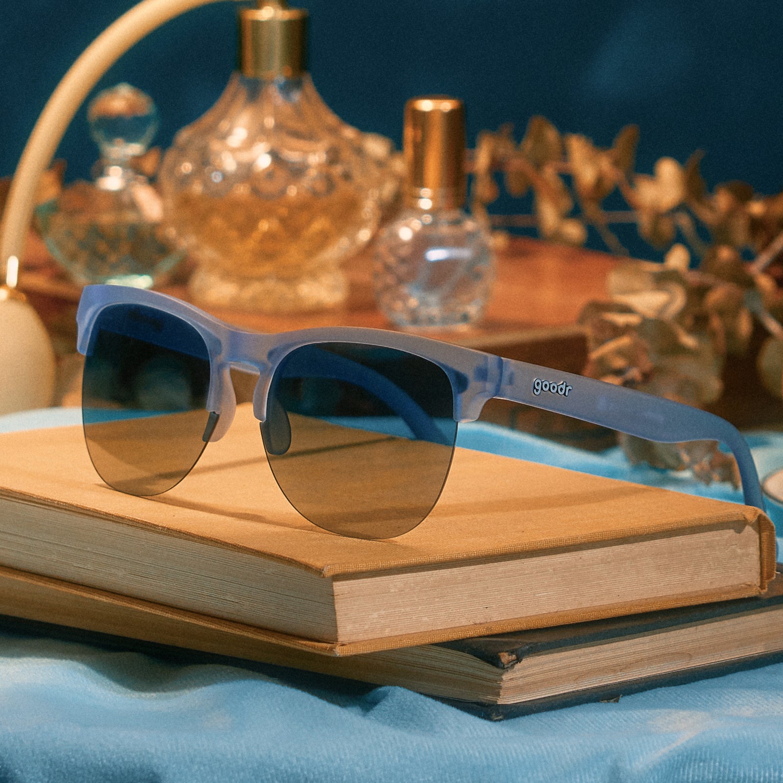A pair of dusty blue translucent Avant Gs with blue lenses sits atop some vintage books on a pale blue velvety fabric.